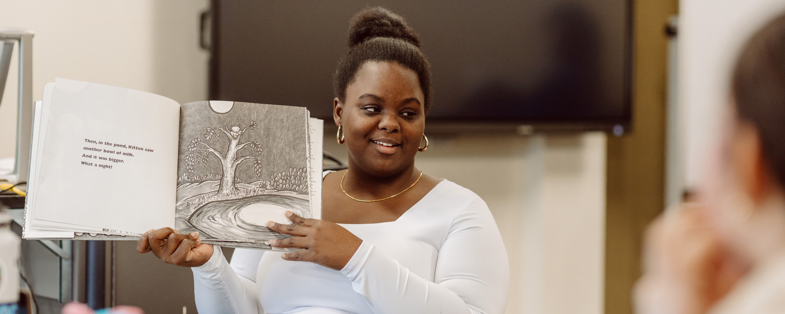 Student holding picture book, reading to classroom